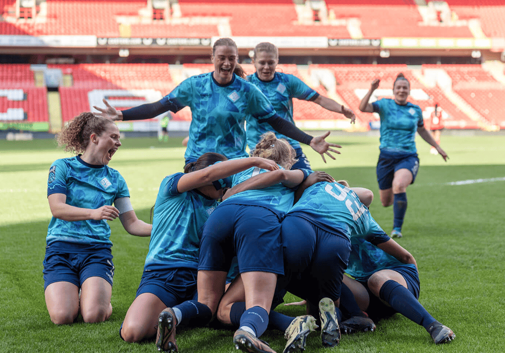 A group of football players from London City Lionesses in blue uniforms celebrating a goal with joy and excitement on the pitch. 