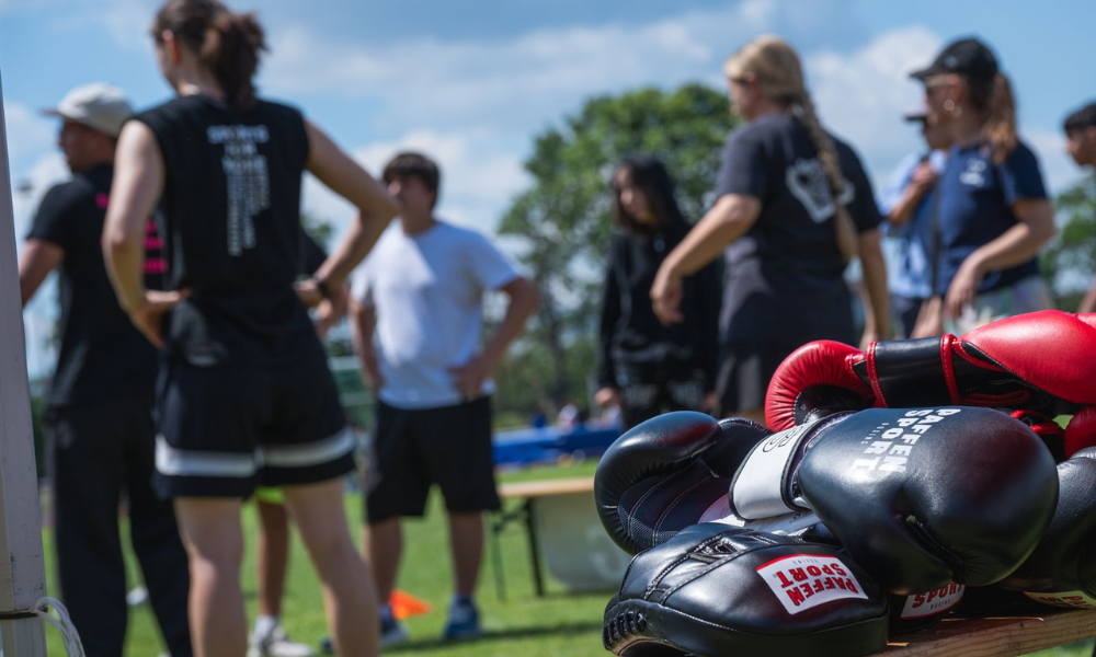 in the foreground, pairs of boxing gloves sit on a bench, in the background, young female athletes get ready to practice